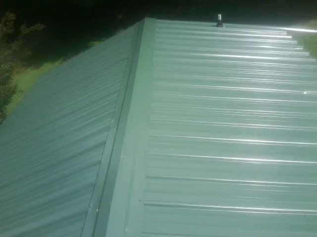 New green metal panels meeting at the ridge of a roof — Flat Roof Repair work by our crew in Milton